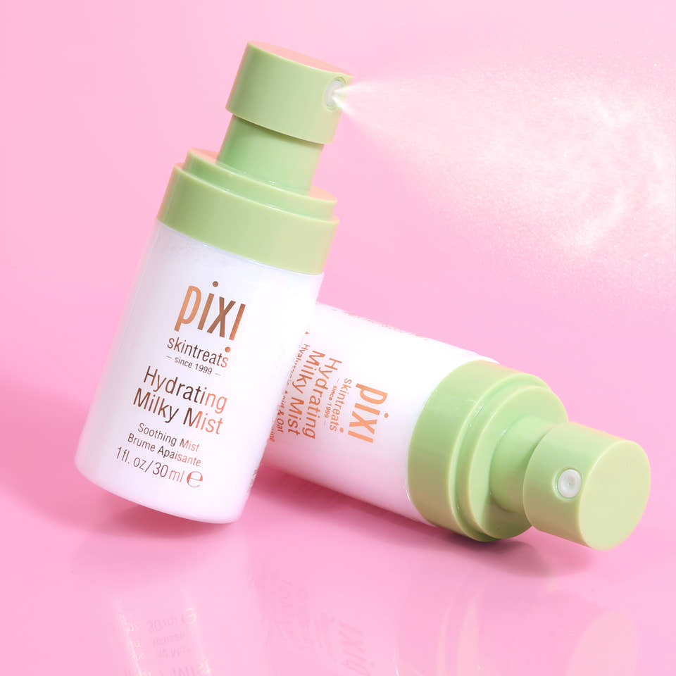 Pixi Skintreats Hydrating Milky Mist Petites bottle shown upright and lying on its side on a pink reflective surface, with mist visible from the pump. view 1